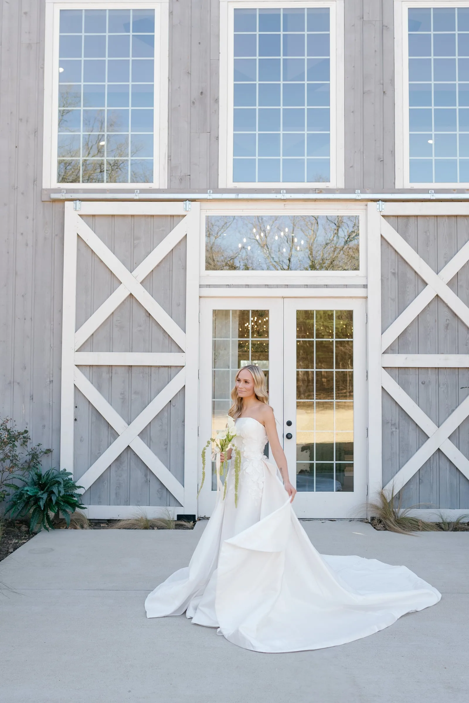 Bride sweeping her gown before the gray barn doors of a Texas wedding venue