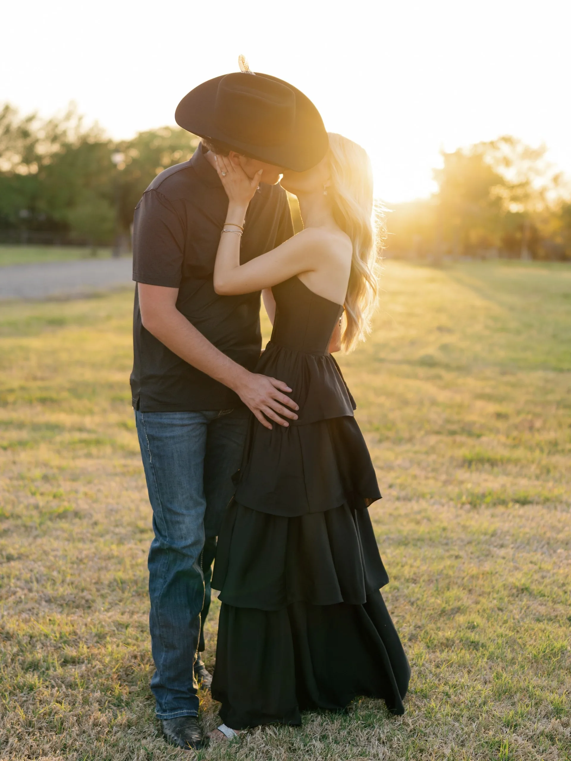 Couple embracing in warm evening light, black cowboy hat and tiered black dress