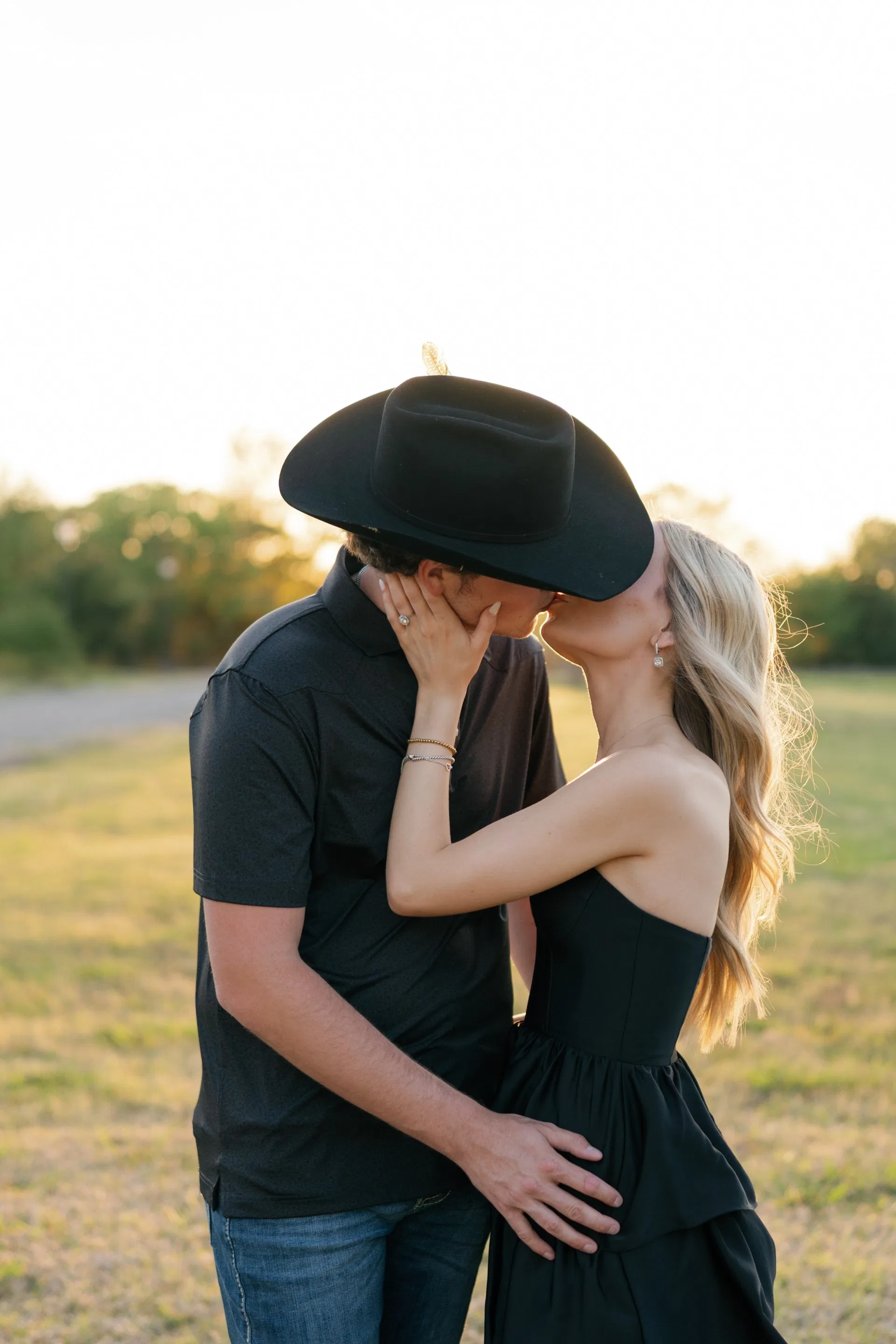 Couple kissing under a wide-brim cowboy hat in a golden Texas field