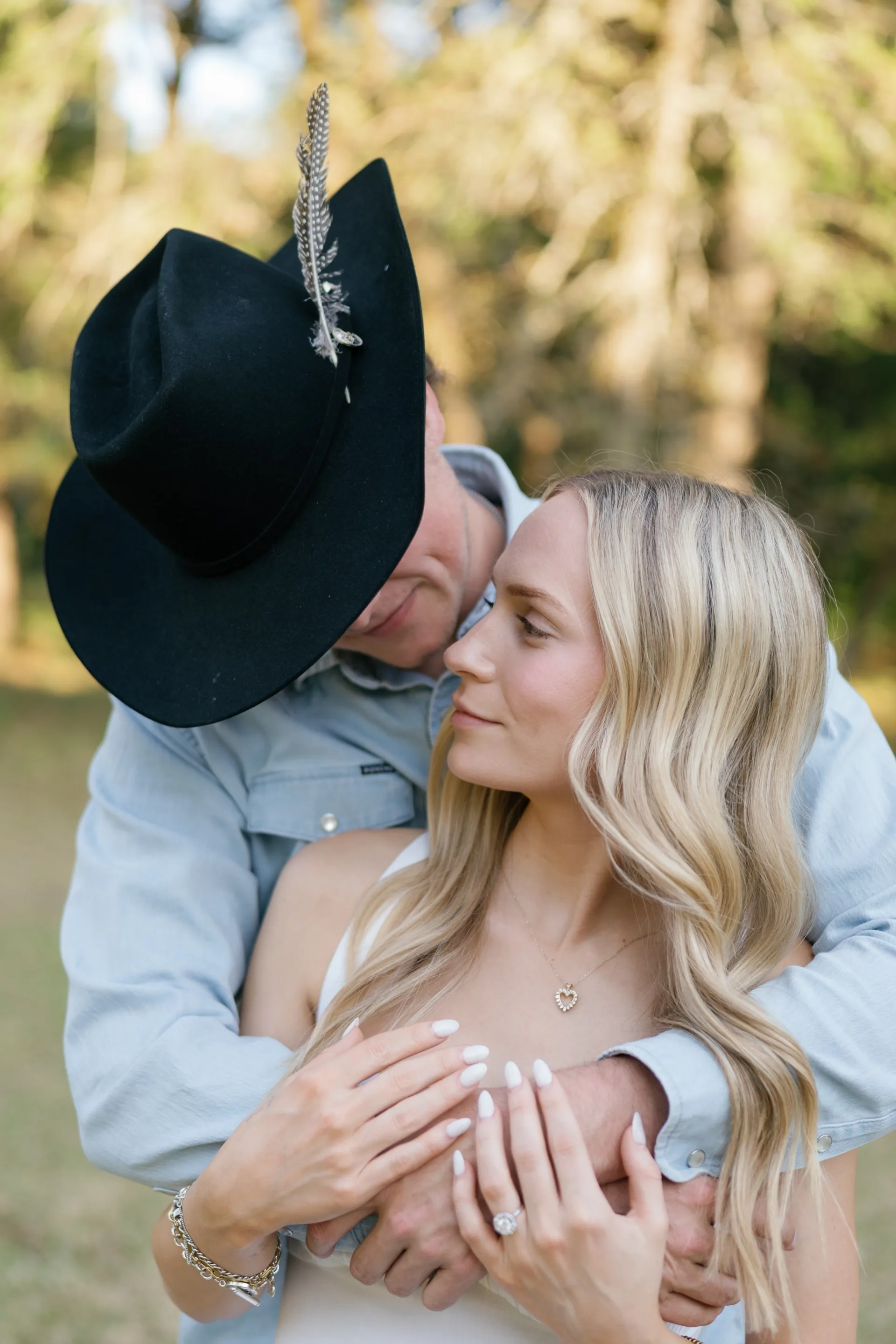 Close embrace under a black felt cowboy hat during a countryside engagement session