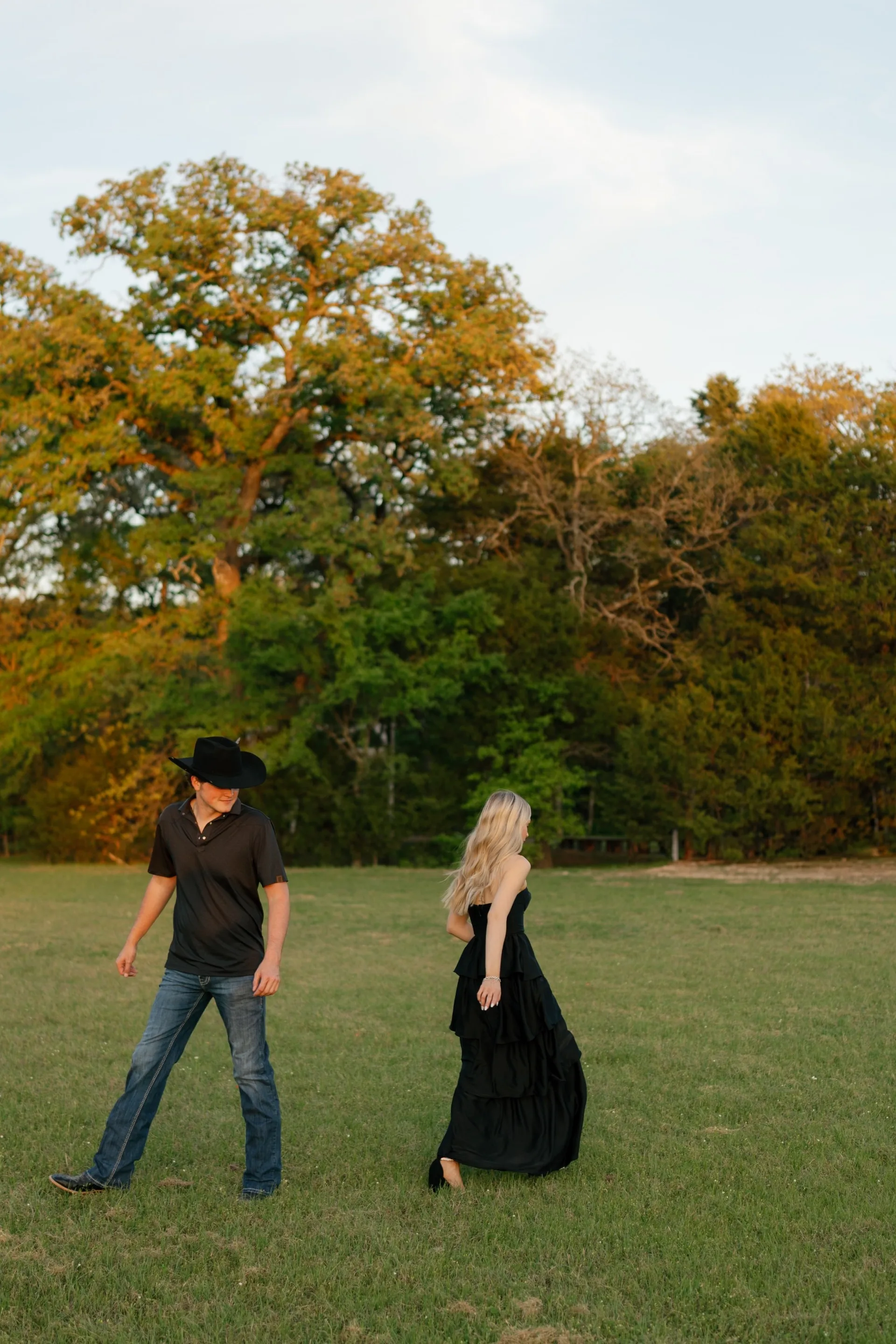 Couple in black western wear walking through a green pasture at last light