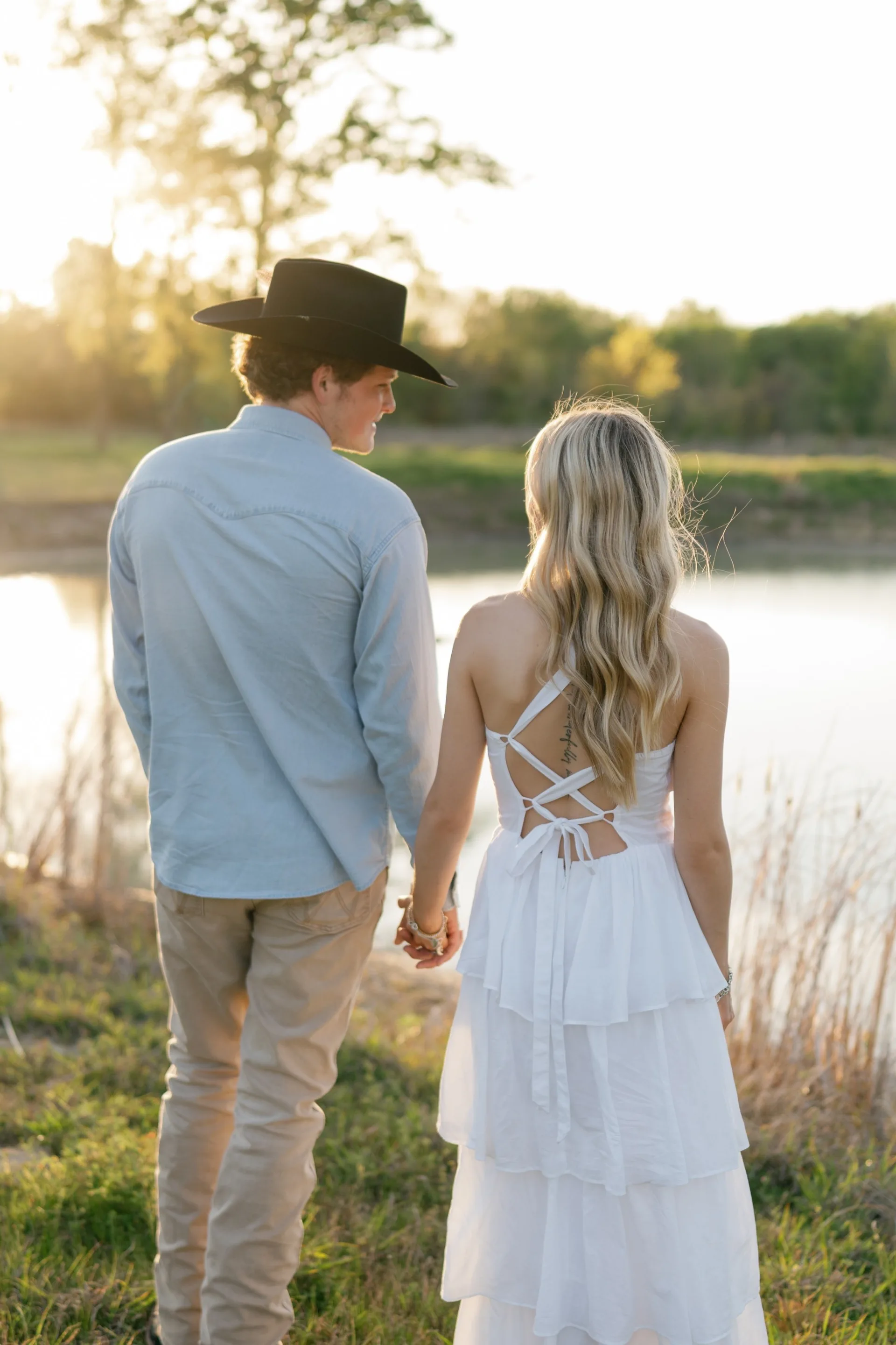 Engaged couple holding hands at the water's edge in warm DFW evening light