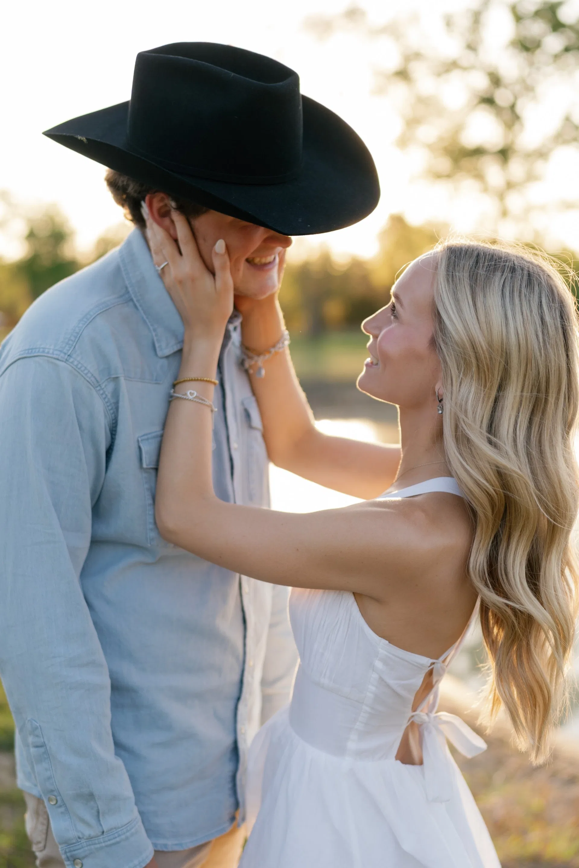 She cradles his face beneath a black cowboy hat in golden evening light