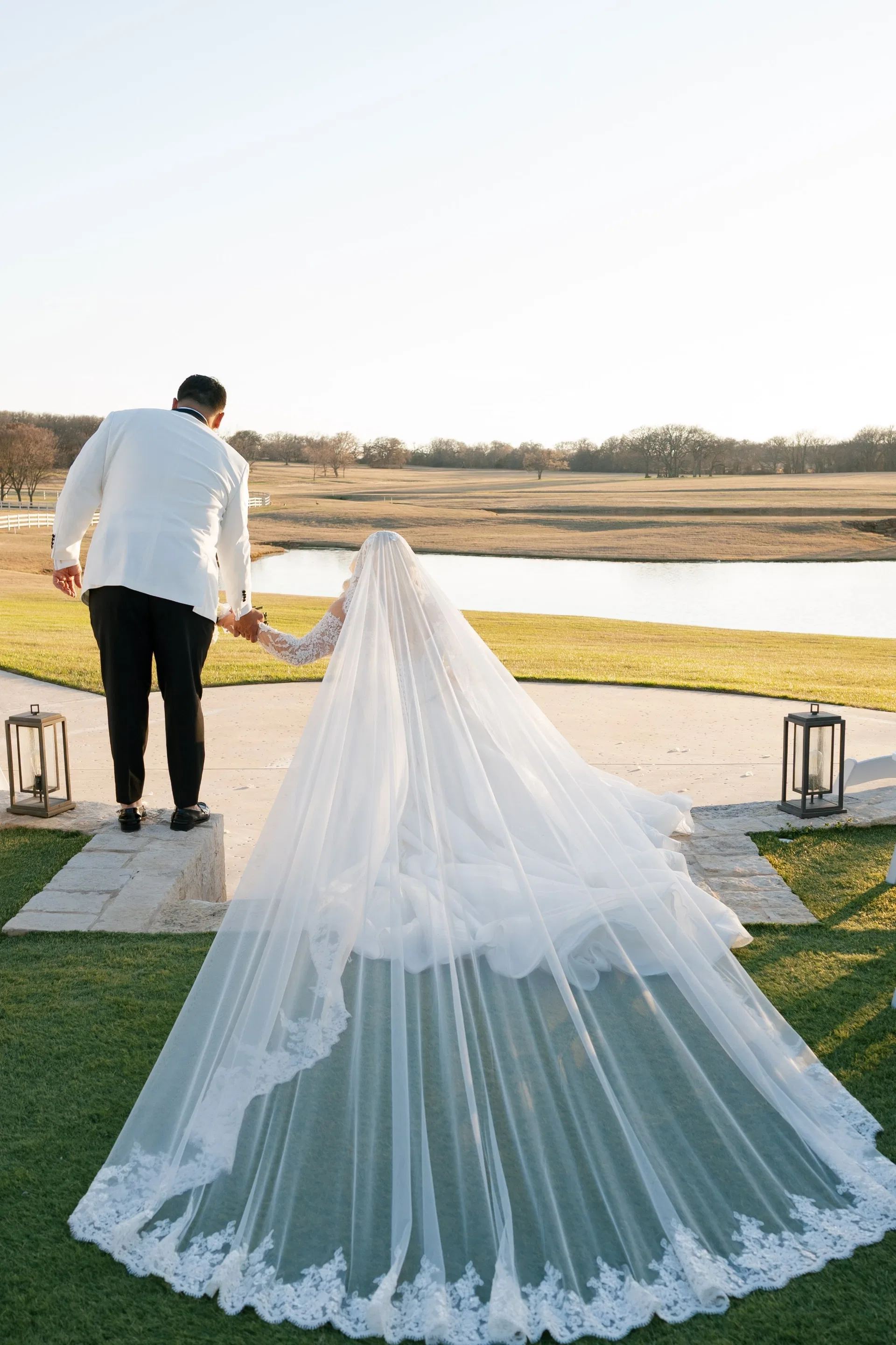 Cathedral veil fanned across the stone walkway as the couple faces the pond