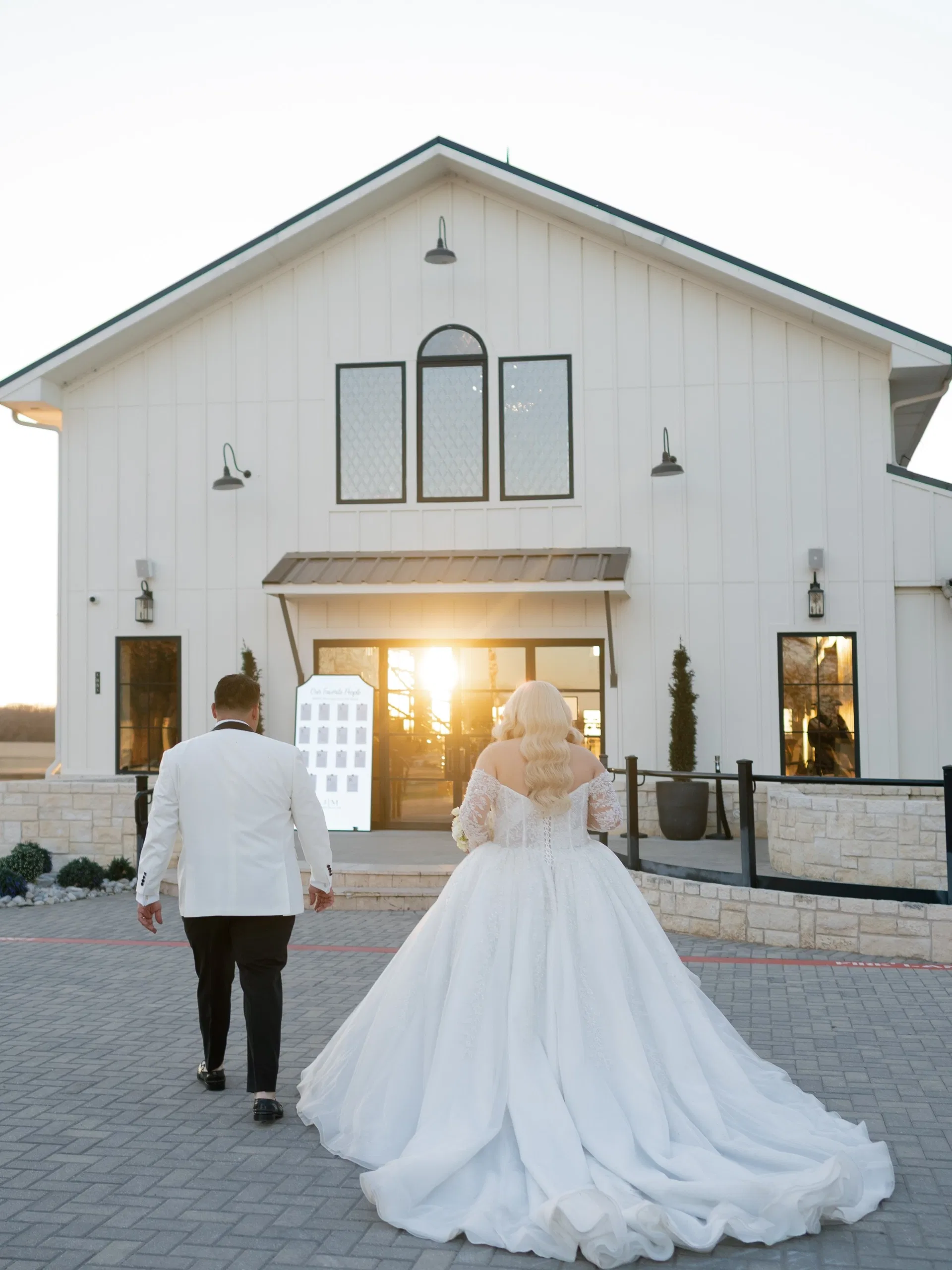 Newlyweds walking toward a white barn venue glowing at sunset, DFW intimate wedding