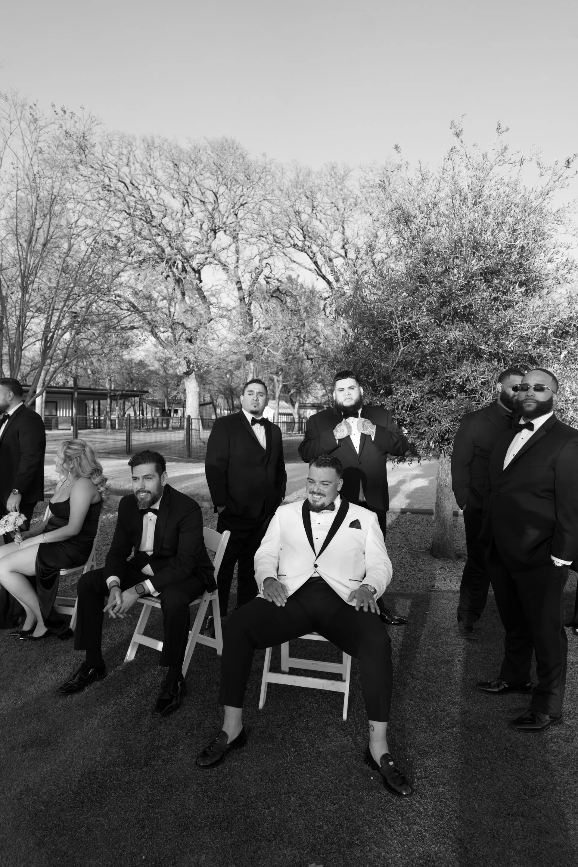 Groom in white tuxedo jacket seated among groomsmen in a monochrome editorial portrait