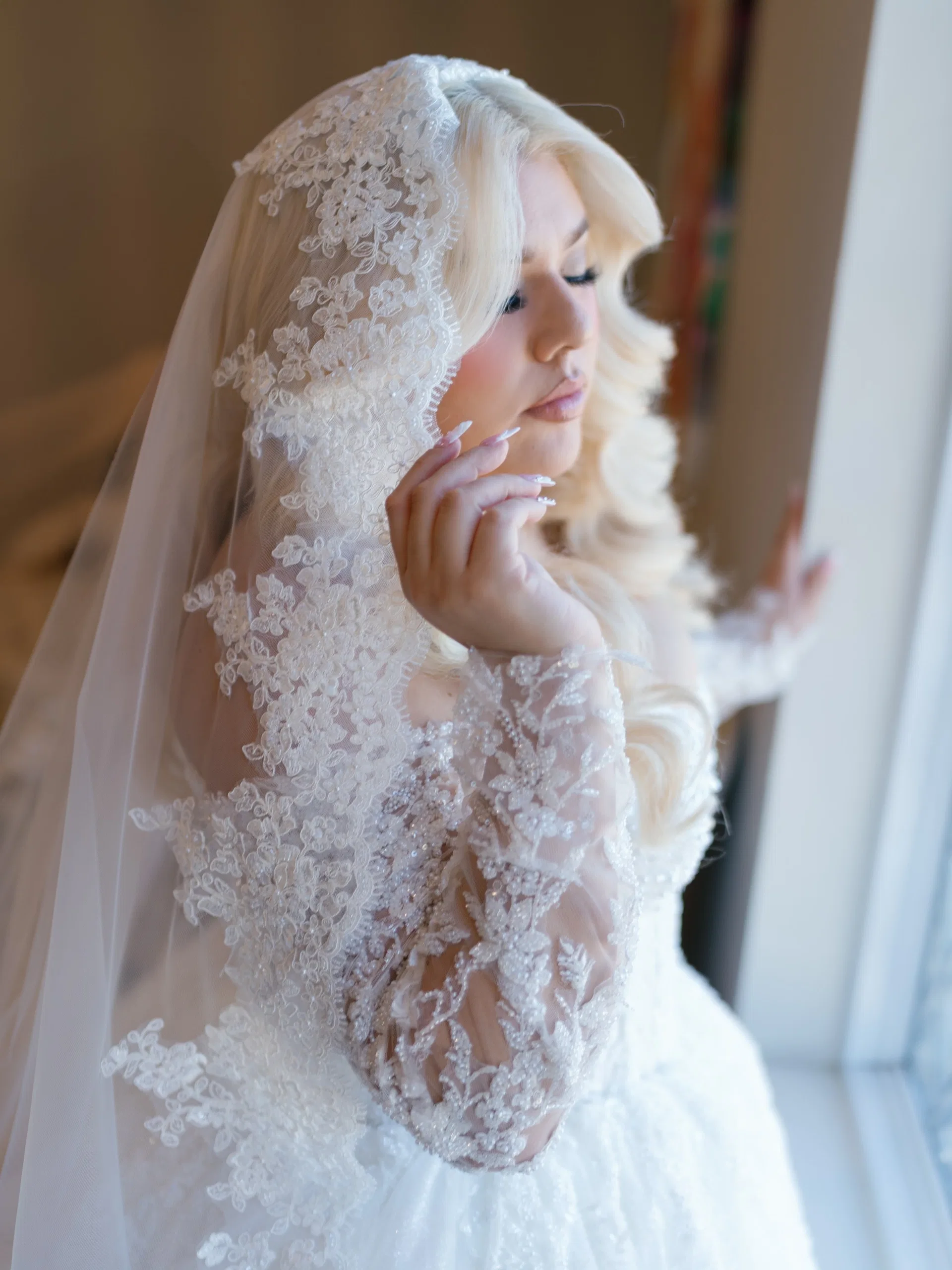 Bride draped in a lace-trimmed veil pausing in soft window light