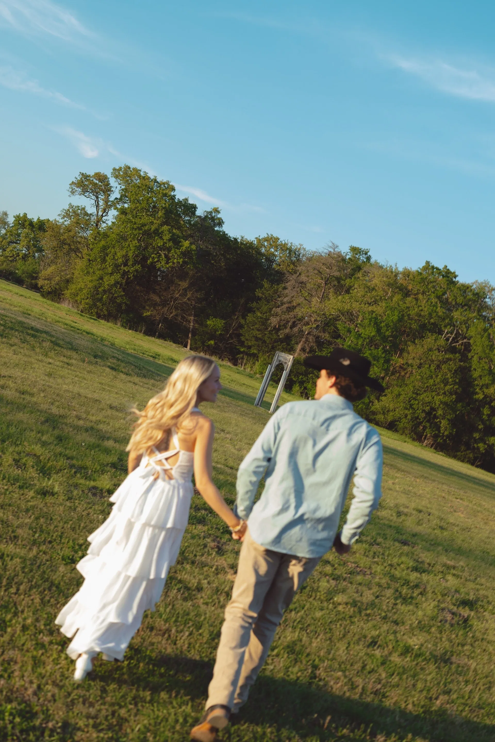Engaged couple walking hand in hand up a sunny Texas pasture hill