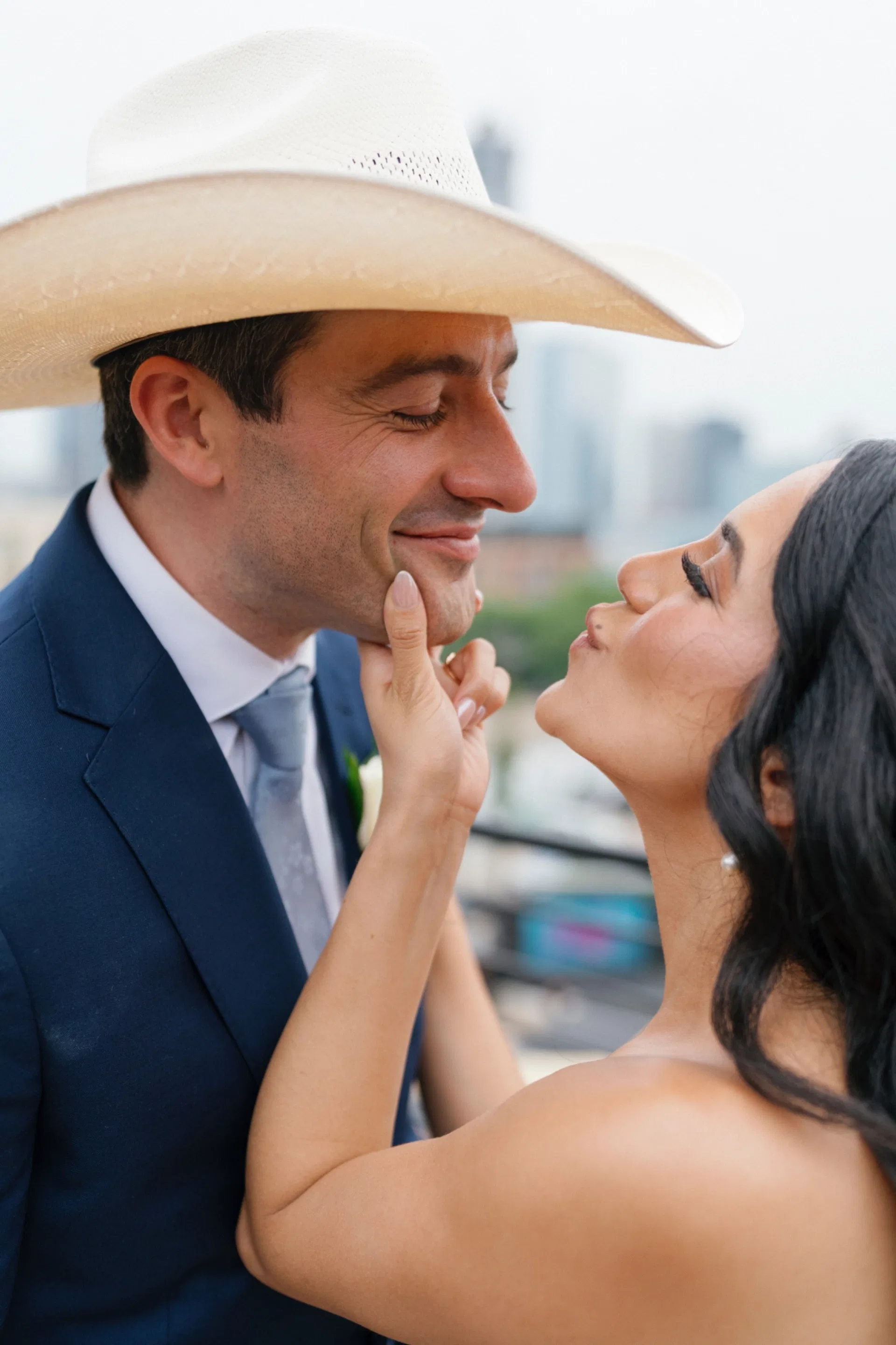 Bride pulling her cowboy-hatted groom close against a hazy Dallas skyline