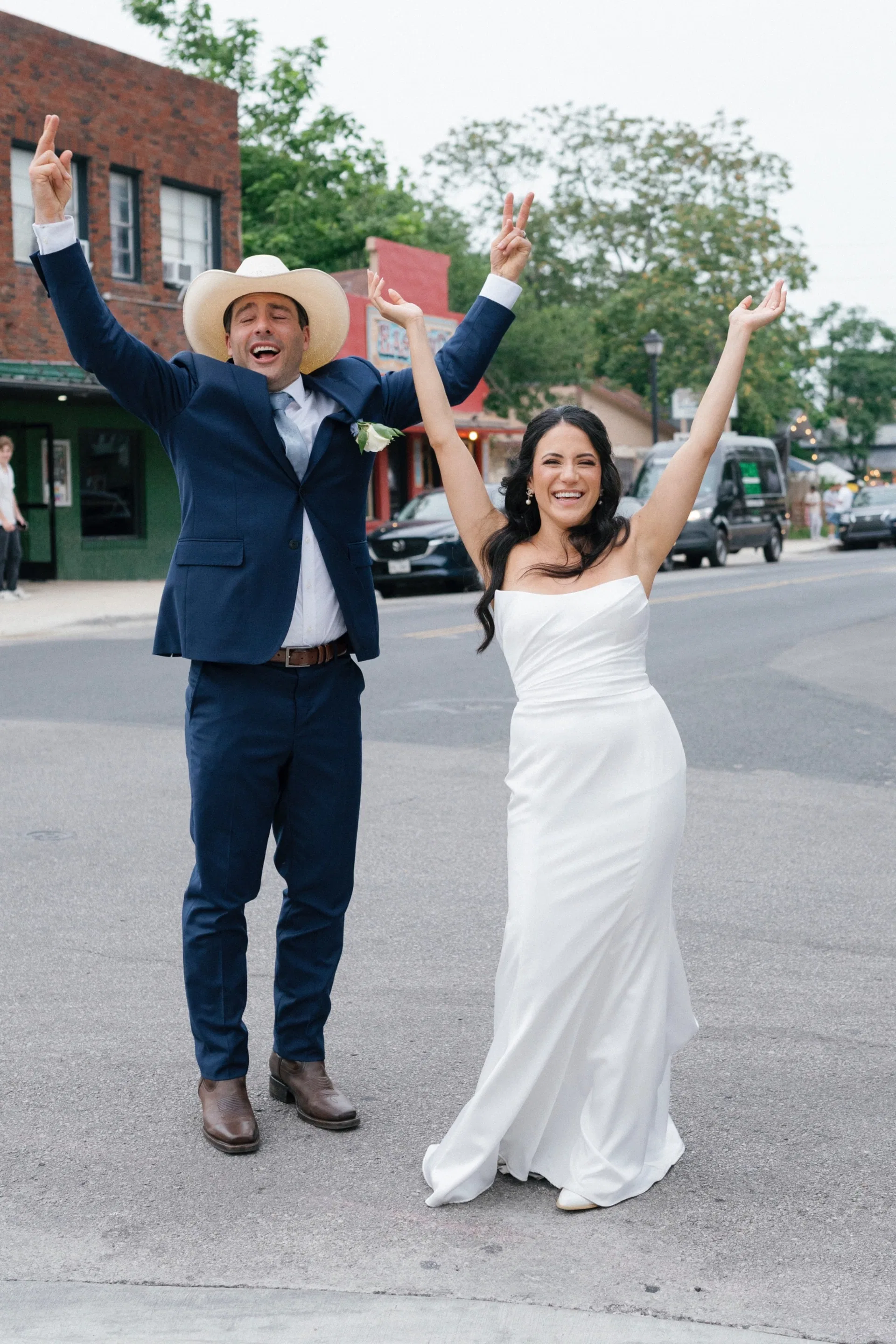 Newlyweds cheering with arms raised in the middle of a Dallas street after eloping