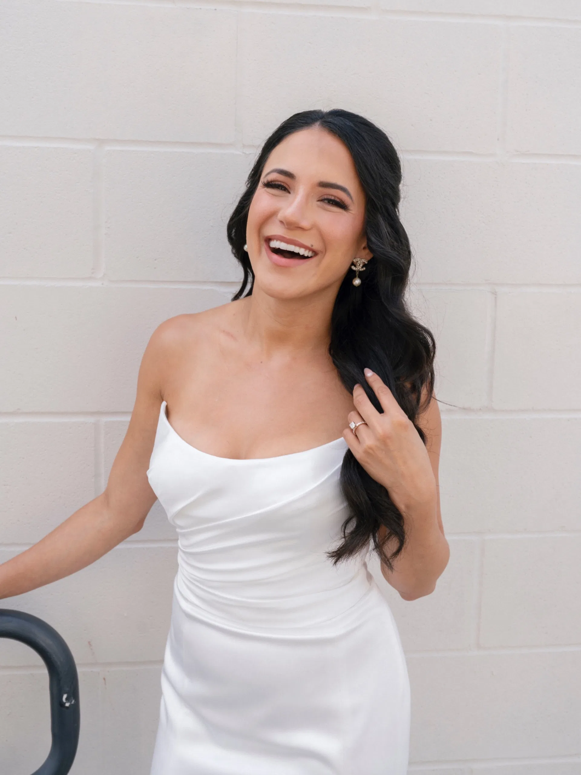 Bride in a strapless satin gown laughing against a white brick wall in Dallas