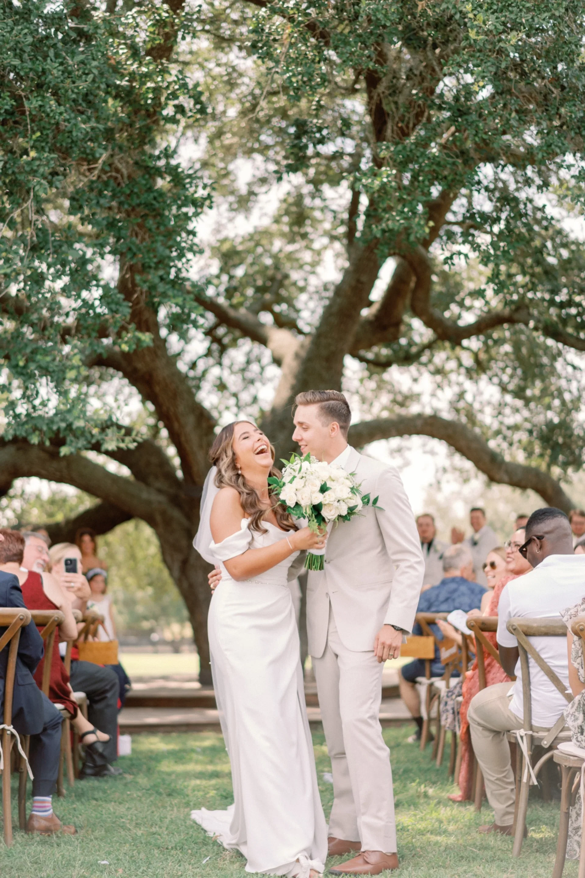 Bride laughing beside her groom under a sprawling live oak at their Texas ceremony