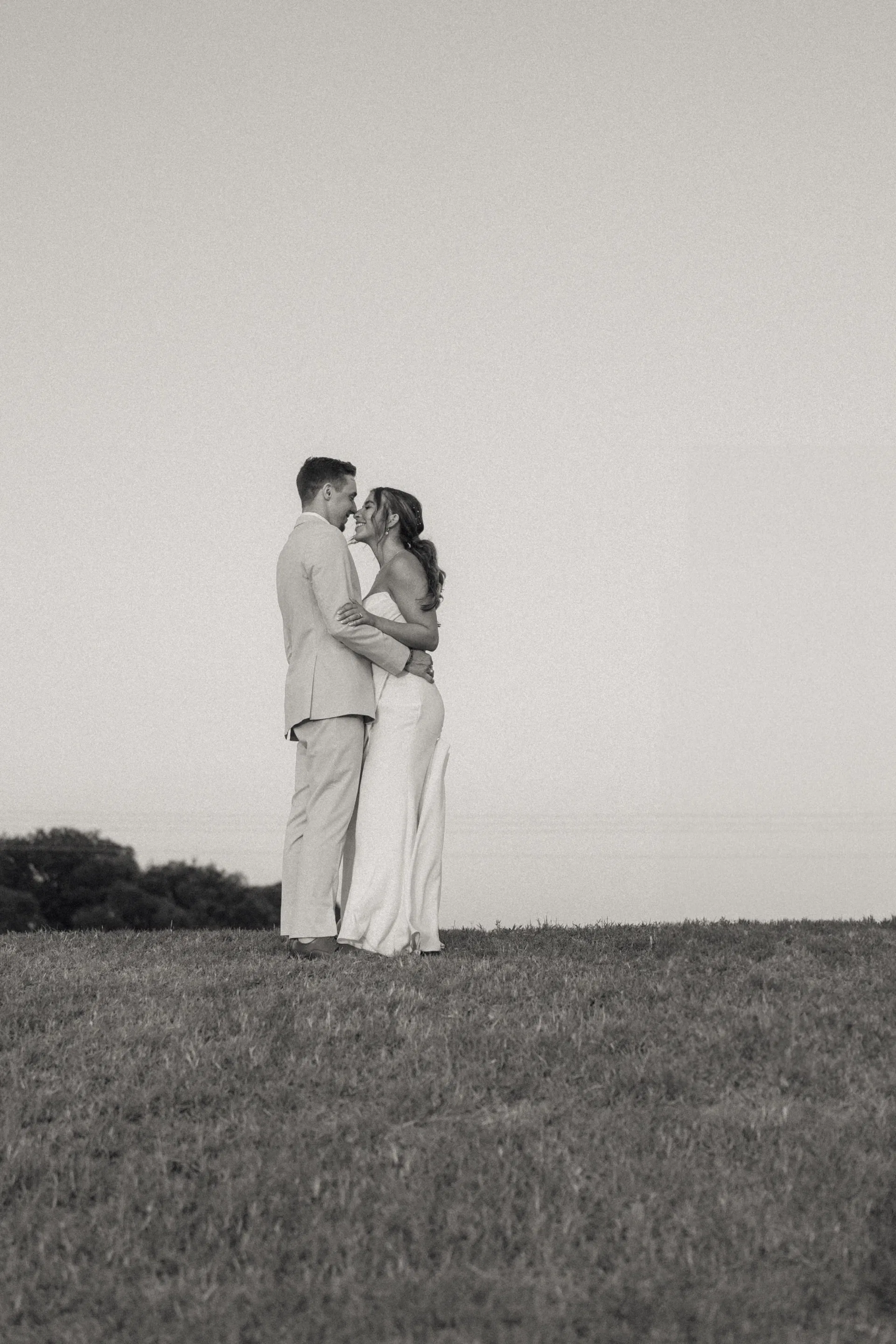 Black-and-white portrait of newlyweds nose to nose on a quiet open hilltop
