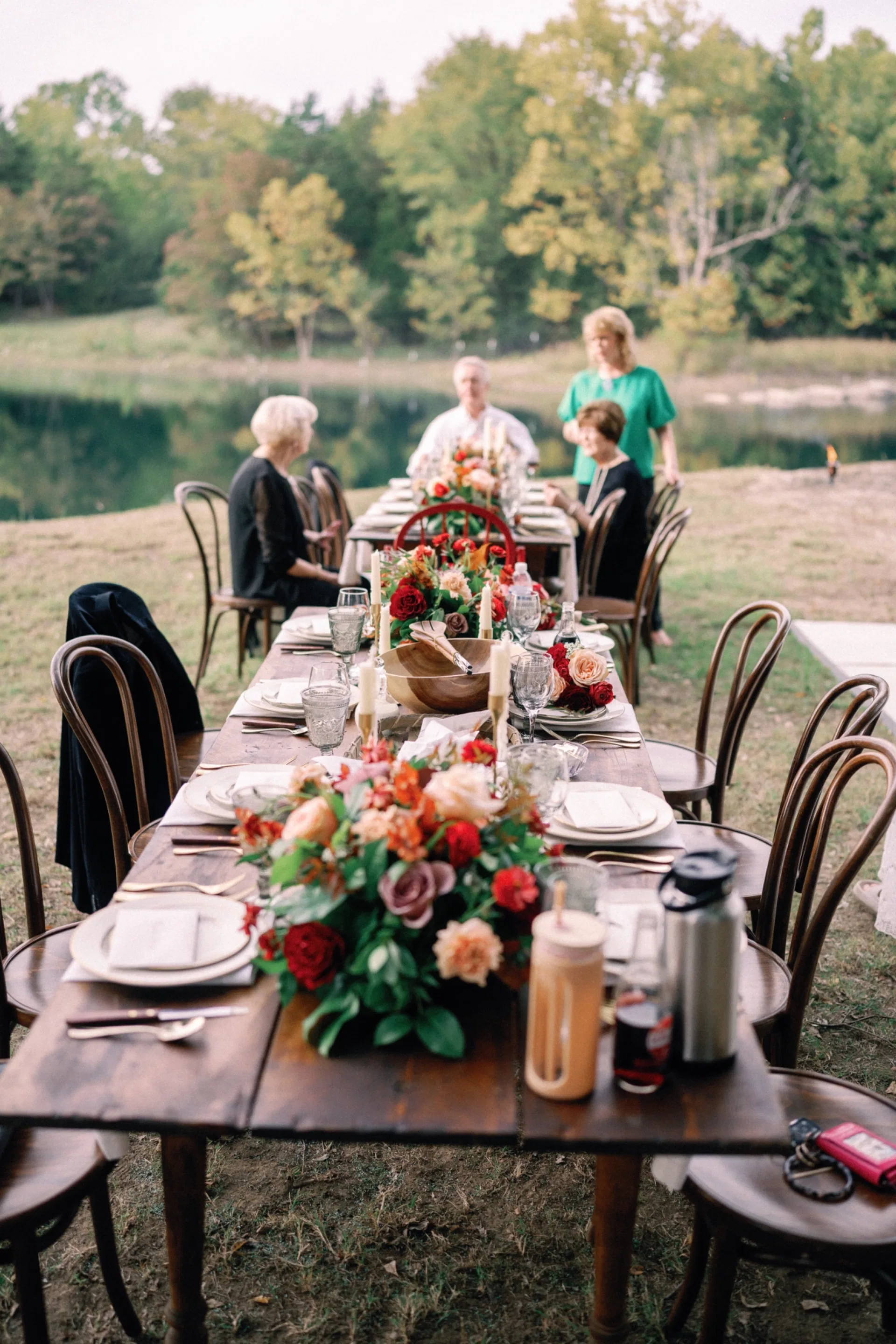 Family gathered at a lakeside farm table dressed with autumn roses and candles