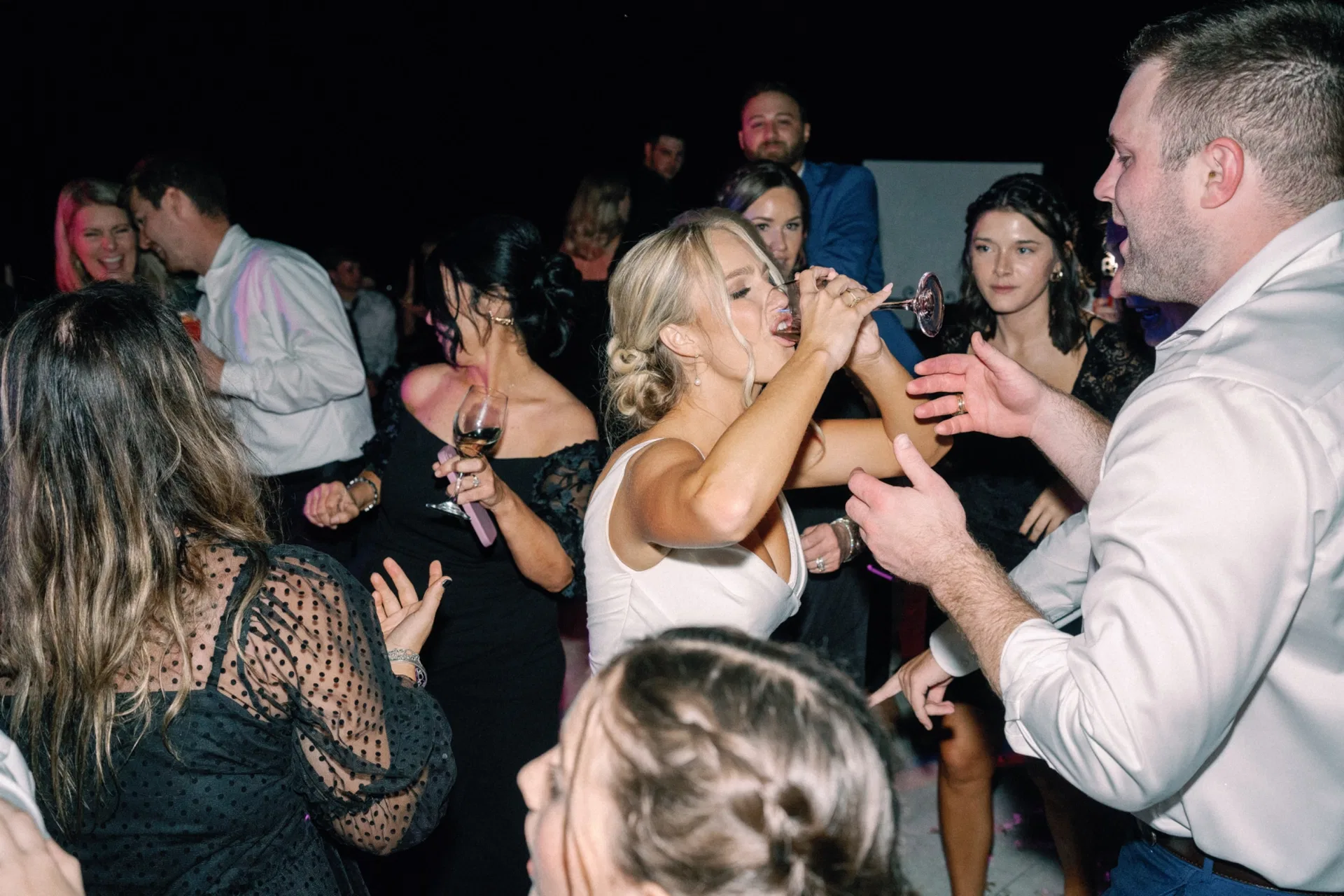Bride sipping a cocktail mid-song on a packed Dallas wedding dance floor